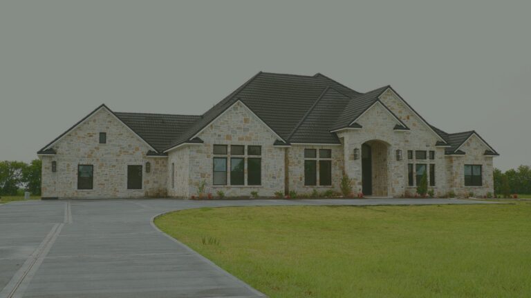 Front of Needville Cottage, a single-story stone home with a dark roof, a curved driveway and a green lawn.