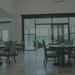 Bright dining room at Needville Cottage with round tables, upholstered chairs, a stone fireplace and glass doors to a sunroom.