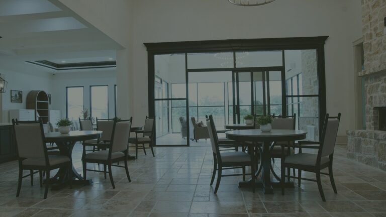 Bright dining room at Needville Cottage with round tables, upholstered chairs, a stone fireplace and glass doors to a sunroom.