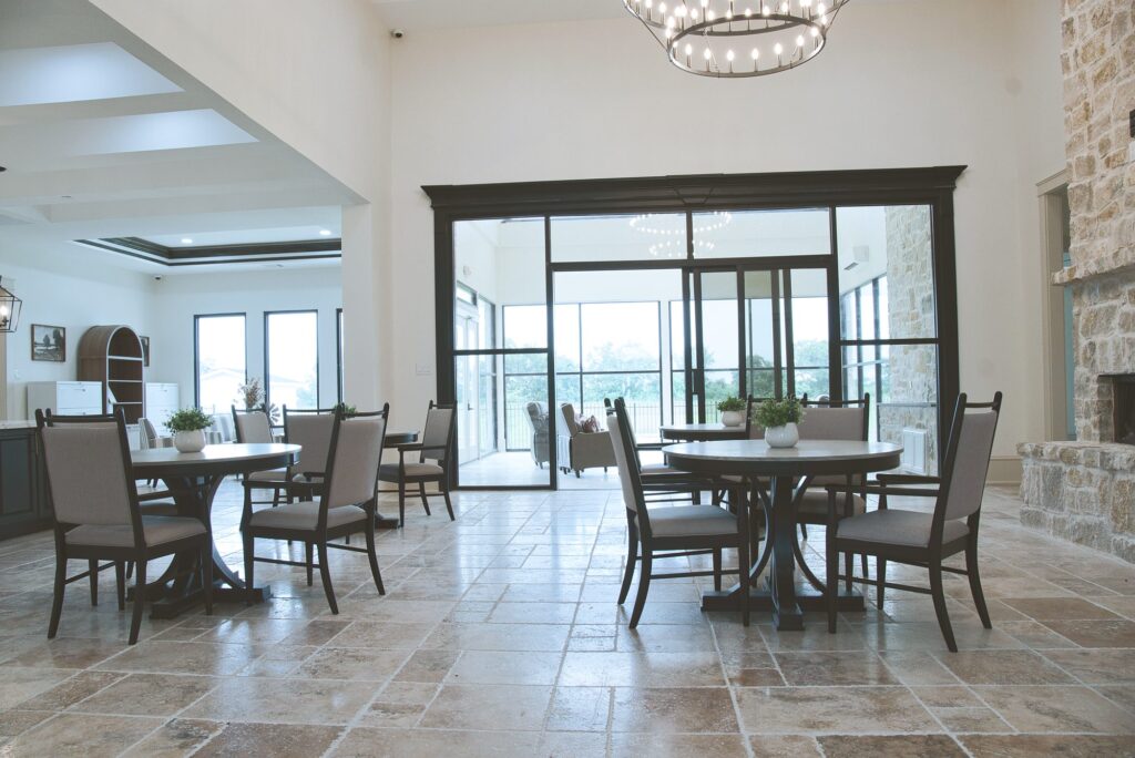 Dining tables beside a stone fireplace and a glass wall that opens to the sunroom in the Needville home