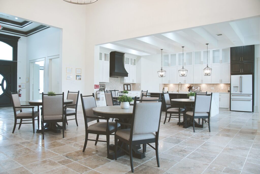 Dining room with round tables and an open kitchen at the Needville assisted living home