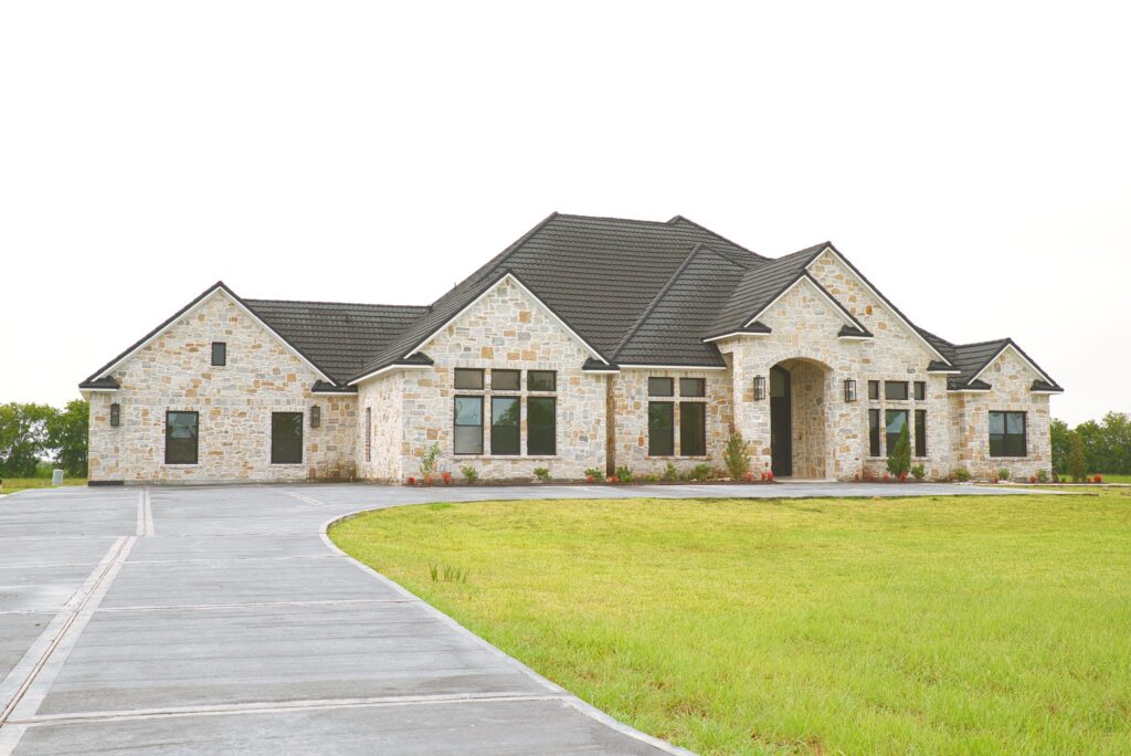 Front of the Village Forest Care Cottage assisted living home in Needville, TX, with its stone exterior and curved driveway