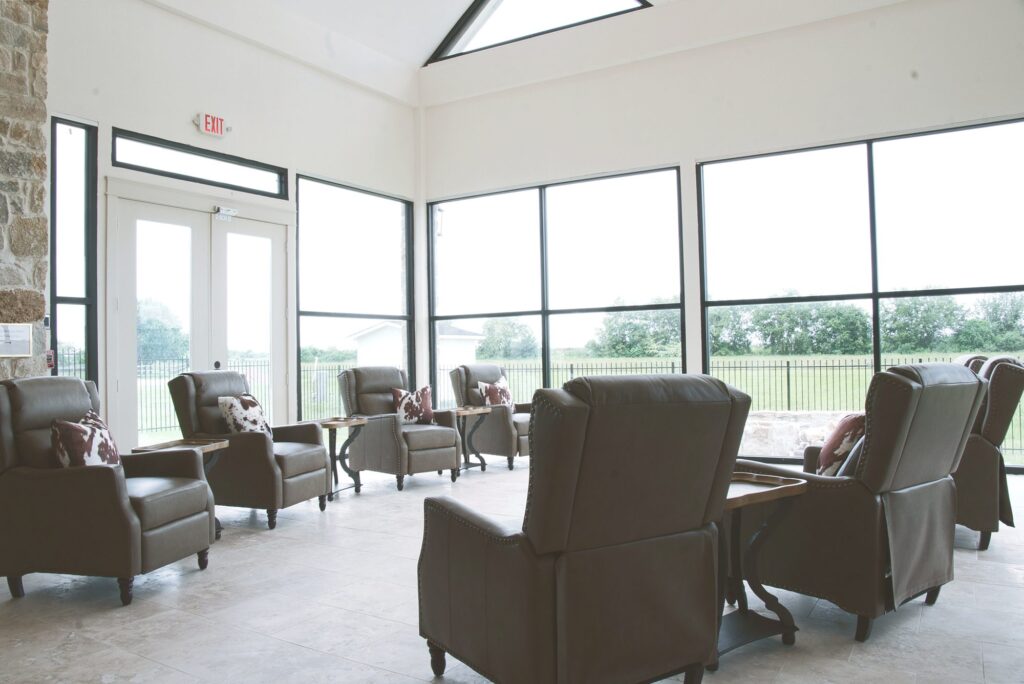 Sunroom with leather recliners and floor-to-ceiling windows at Village Forest assisted living in Needville, TX