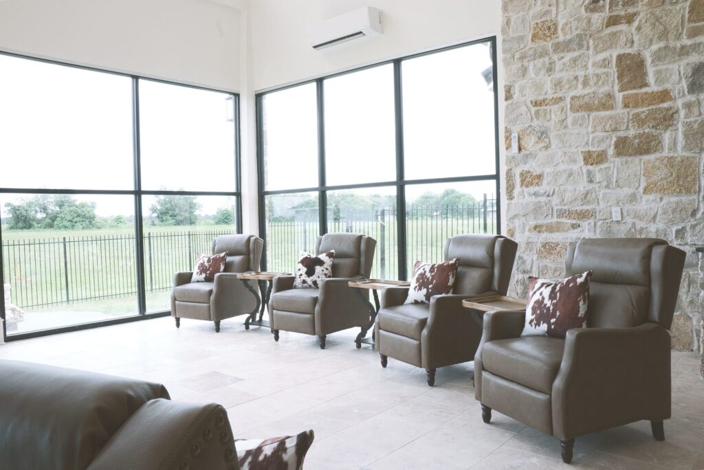 Row of recliners beside a stone wall and tall windows looking out on the fenced yard of the Needville sunroom