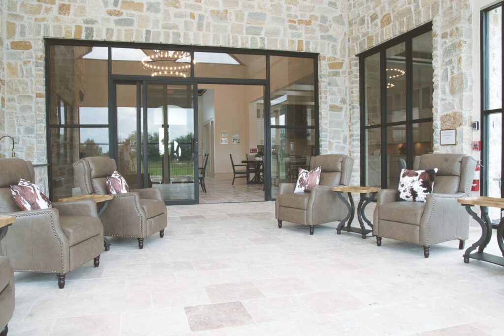Sunroom seating with recliners and cowhide pillows beside a stone wall and glass doors into the dining room at Needville Cottage